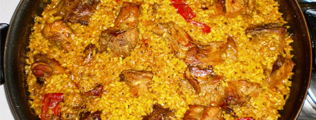Paella de arroz con conejo dorado y tiras de pimiento rojo