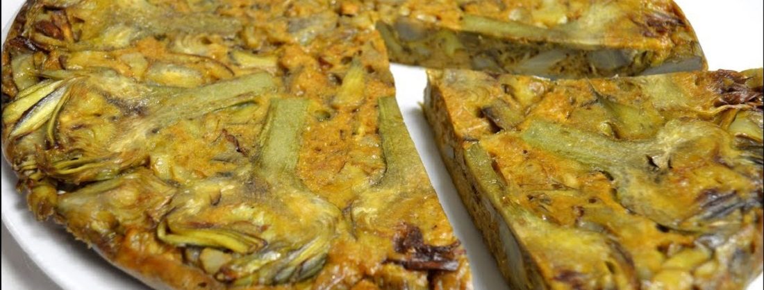 Tortilla de alcachofas dorada servida en una mesa de huerta